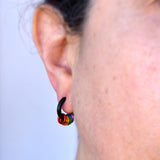 Close-up of a rainbow pride huggie earring in black being worn in an earlobe