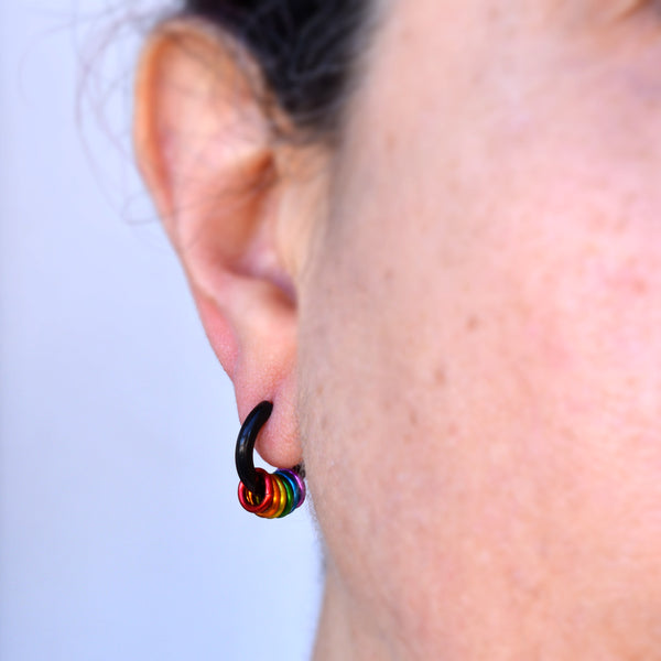 Close-up of a rainbow pride huggie earring in black being worn in an earlobe