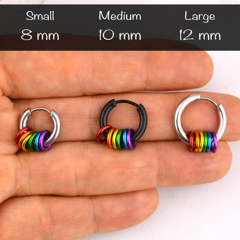 Close-up of three rainbow pride huggie earrings in small 8mm, medium 10mm (black), and large 12mm sizes held in a hand