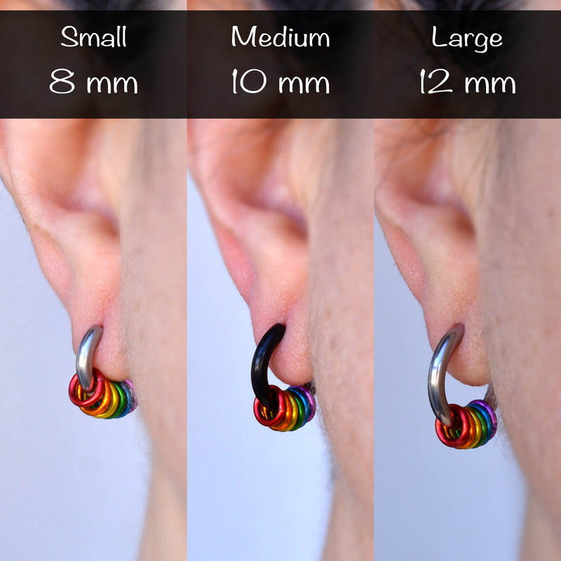 Three earlobes showing rainbow pride huggie earrings in small 8mm (steel), medium 10mm (black), and large 12mm (steel) sizes being worn on an earlobe