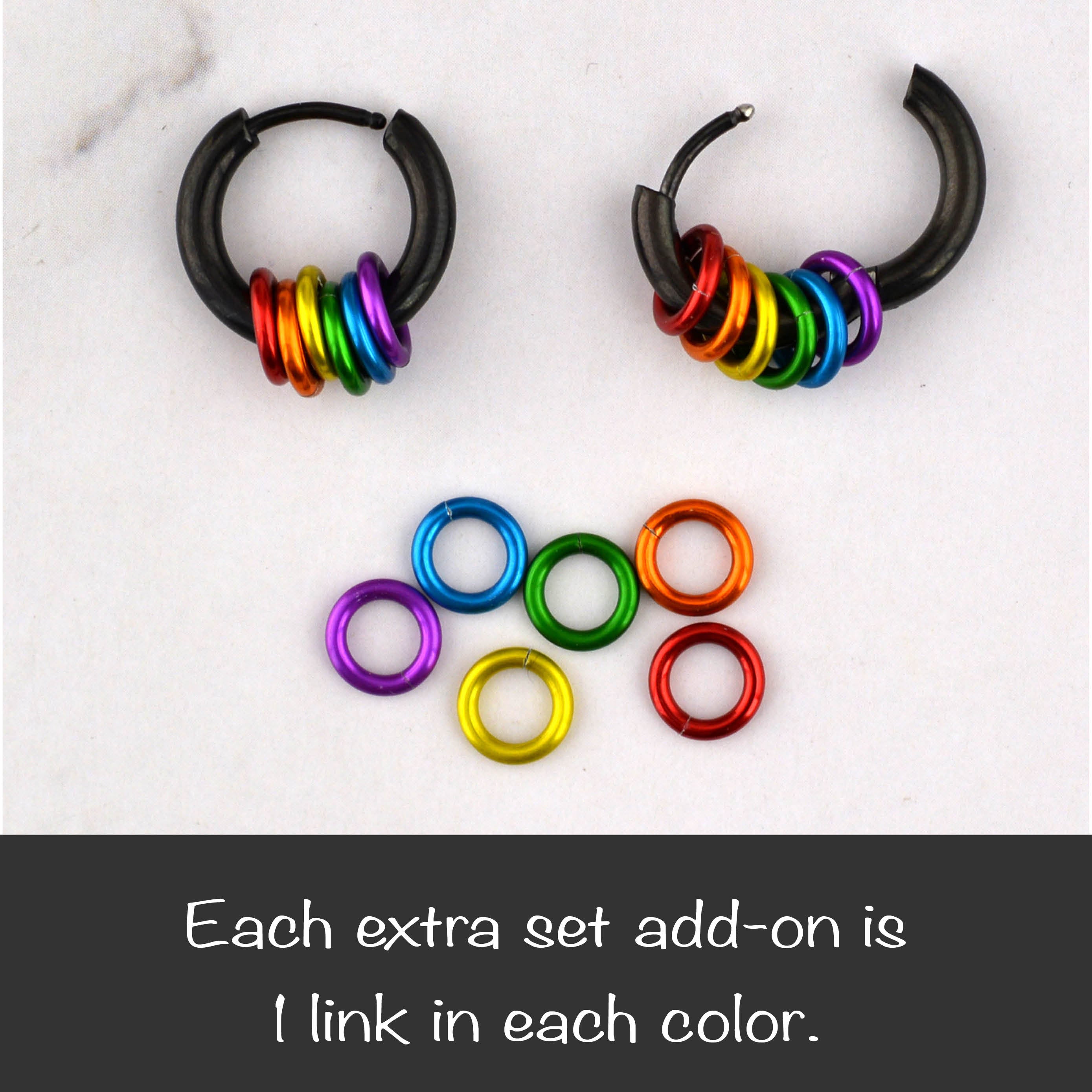 Two black rainbow pride huggie earrings, one open and one closed. Below is a set of six extra colored links (red, orange, gold, green, blue, purple) and text "Each extra set add-on is 1 link in each color."