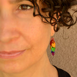 Close-up of Rebeca Mojica, a person with curly dark hair and a warm smile, wearing a "mini" rainbow cascading leaves earring from Rebeca Mojica Jewelry.