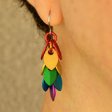 Close-up of a mini Leaf Pride Dangle Earring by Rebeca Mojica Jewelry being worn on an ear. The colorful aluminum leaves are clearly visible.
