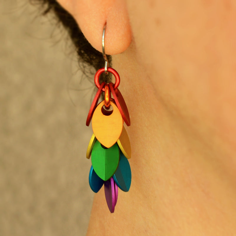 Close-up of a mini Leaf Pride Dangle Earring by Rebeca Mojica Jewelry being worn on an ear. The colorful aluminum leaves are clearly visible.
