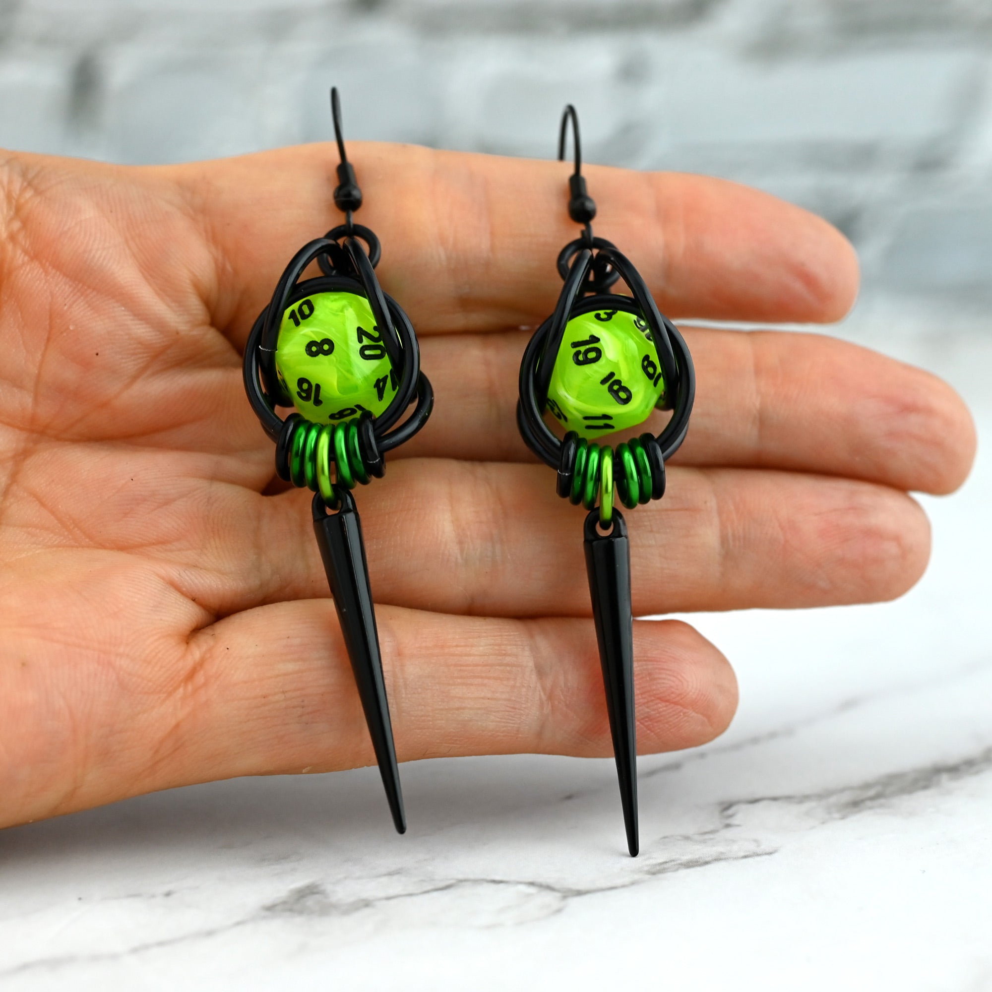 Neon green D20 spike earrings held on a hand to show scale. The miniature dice and 3.25-inch total length are displayed against the palm.
