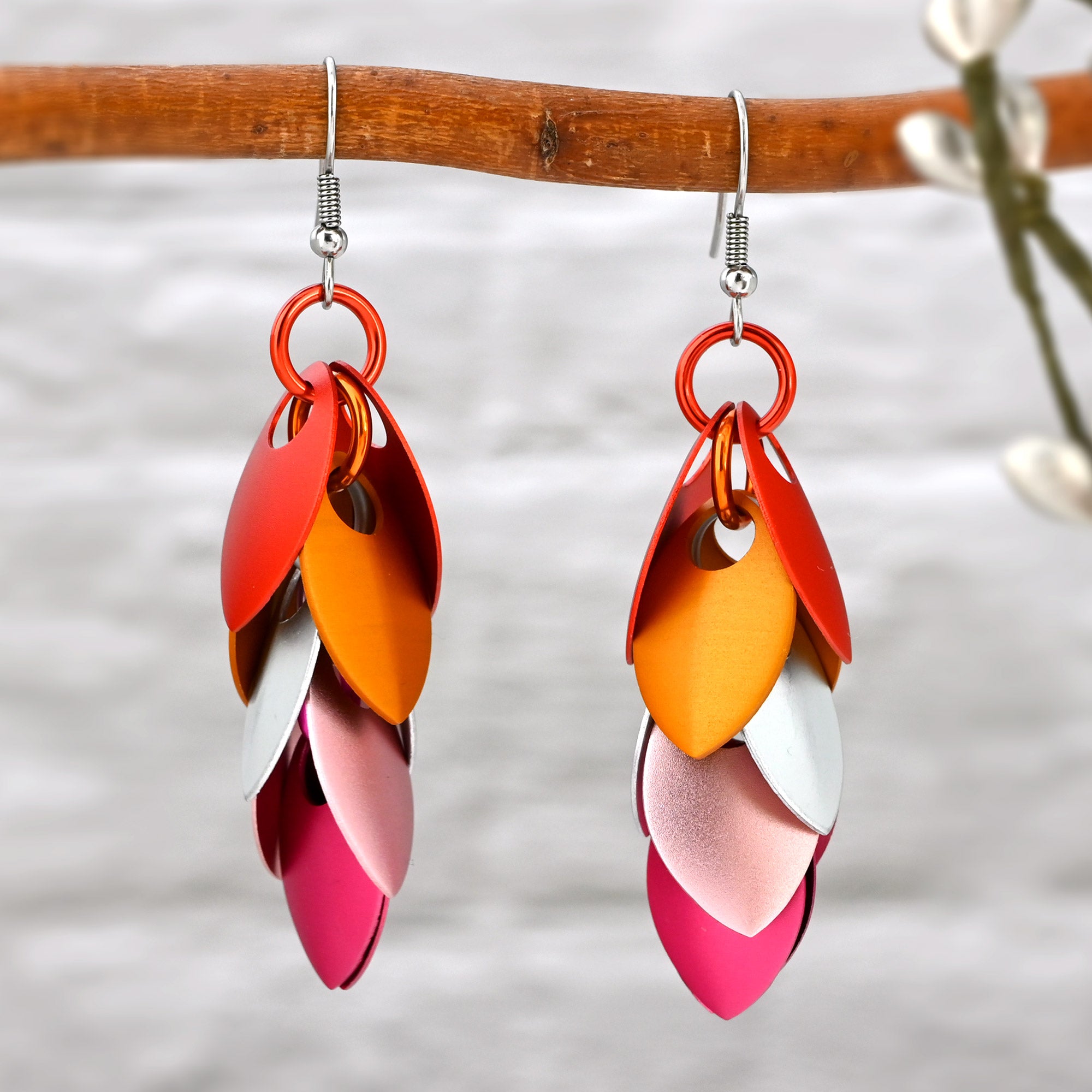 Lesbian Pride cascading leaf earrings hanging from a wooden branch, highlighting the way the scales overlap and dangle.