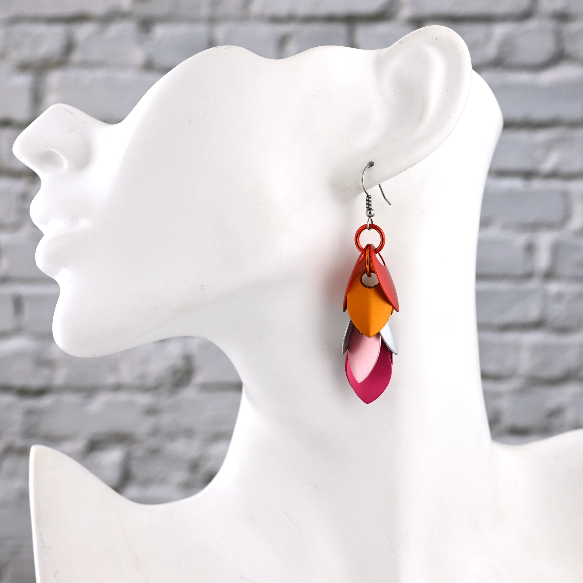 Side profile of a white mannequin bust wearing a long, feathered Lesbian Pride earring, showing how the 3-inch length sits against the neck.