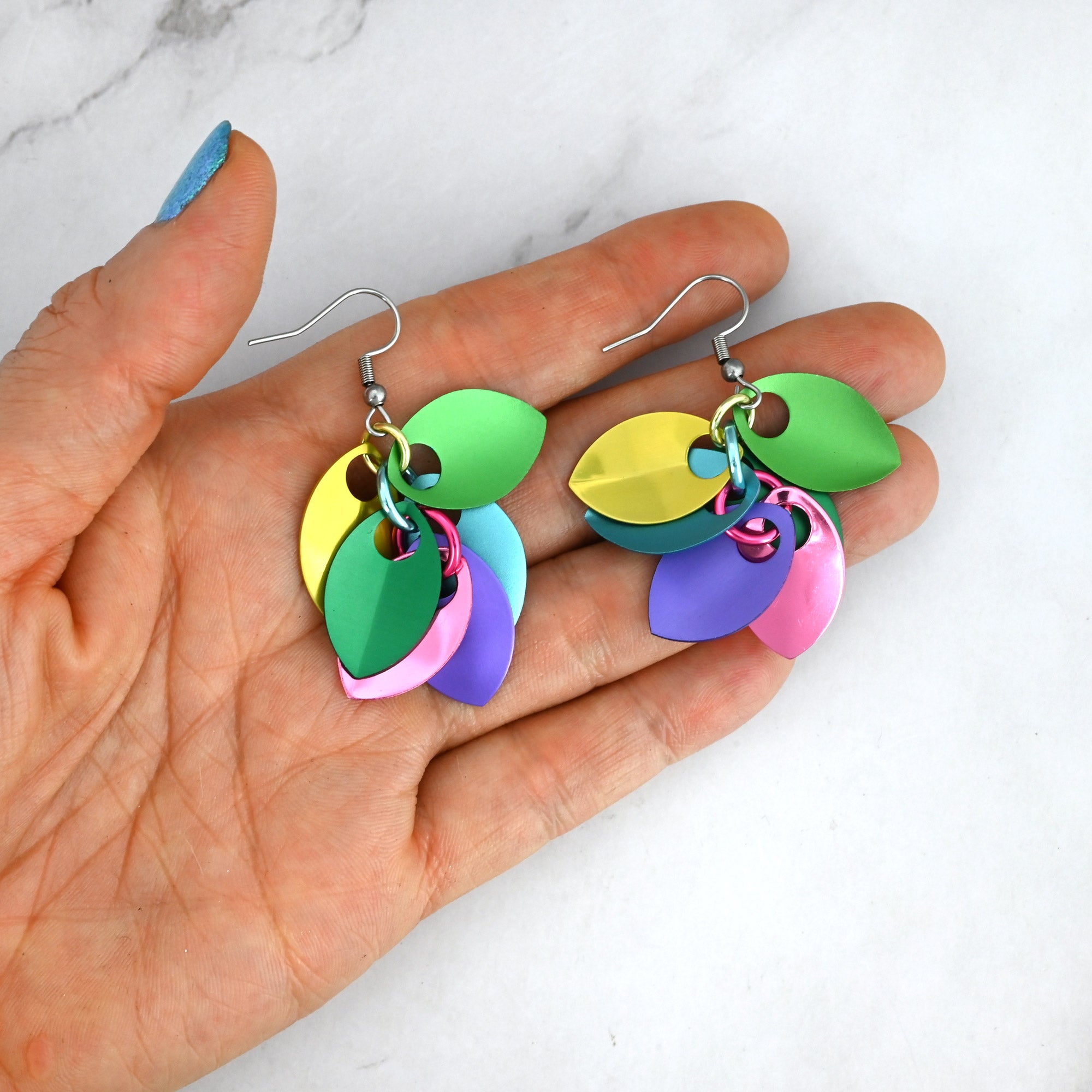 Short scalemaille earrings in a person’s fingertips to showcase their size and rich colors in a mix of saturated pastels. 