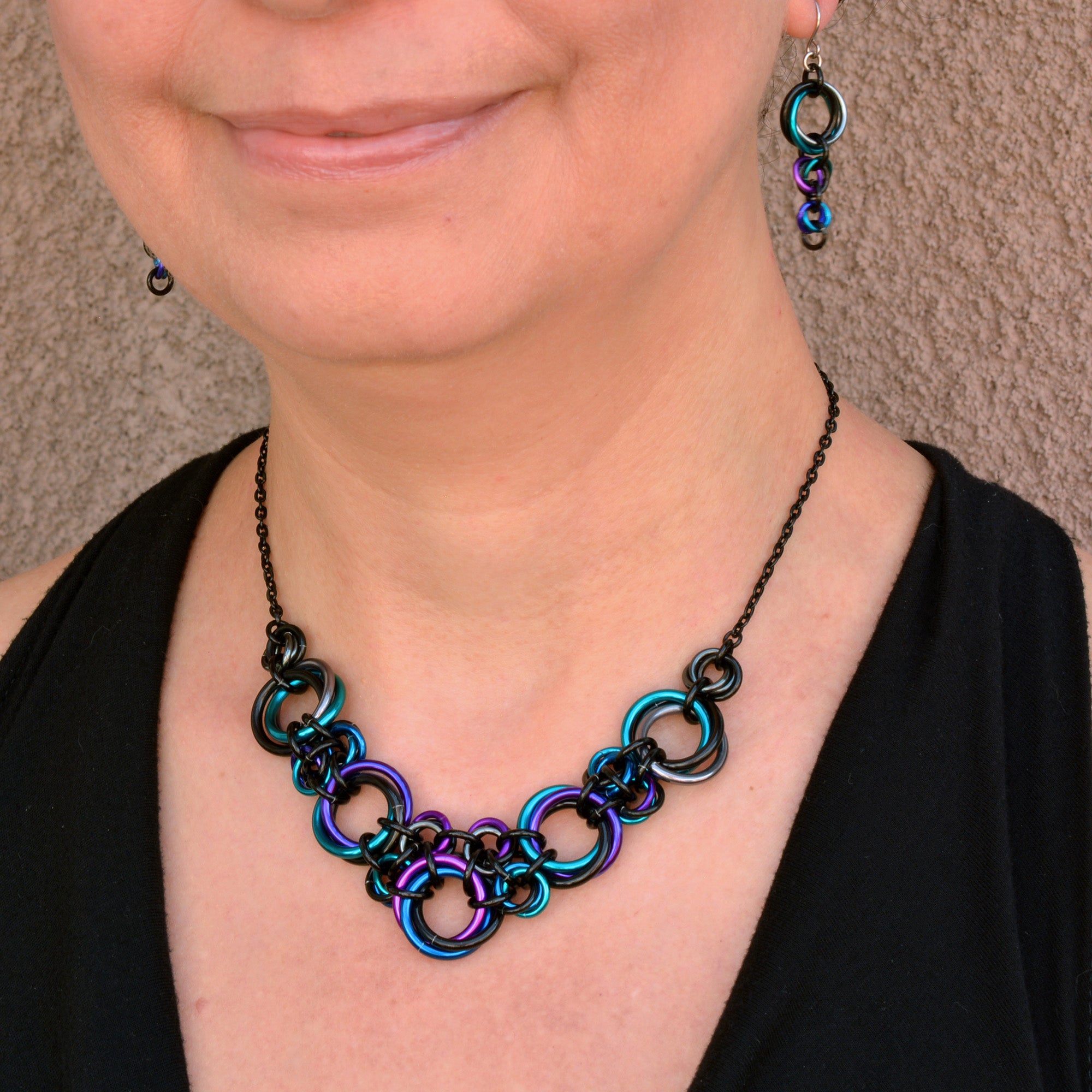 Artisan Rebeca Mojica models the Knotted Metal V necklace (16" length) and matching Comet earrings in Dark Mermaid colors, showcasing the fit.