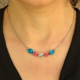 Closeup of short transgender pride chainmaille necklace being worn. Necklace has a 2-inch focal section attached to a thin steel chain on each end. The focal is made of 5 chainmaille “beads” in the Sweet Pea weave - each segment has 6 links of the same color. From left to right, colors are bright blue, pink, white, pink and bright blue - to best match the trans pride flag.