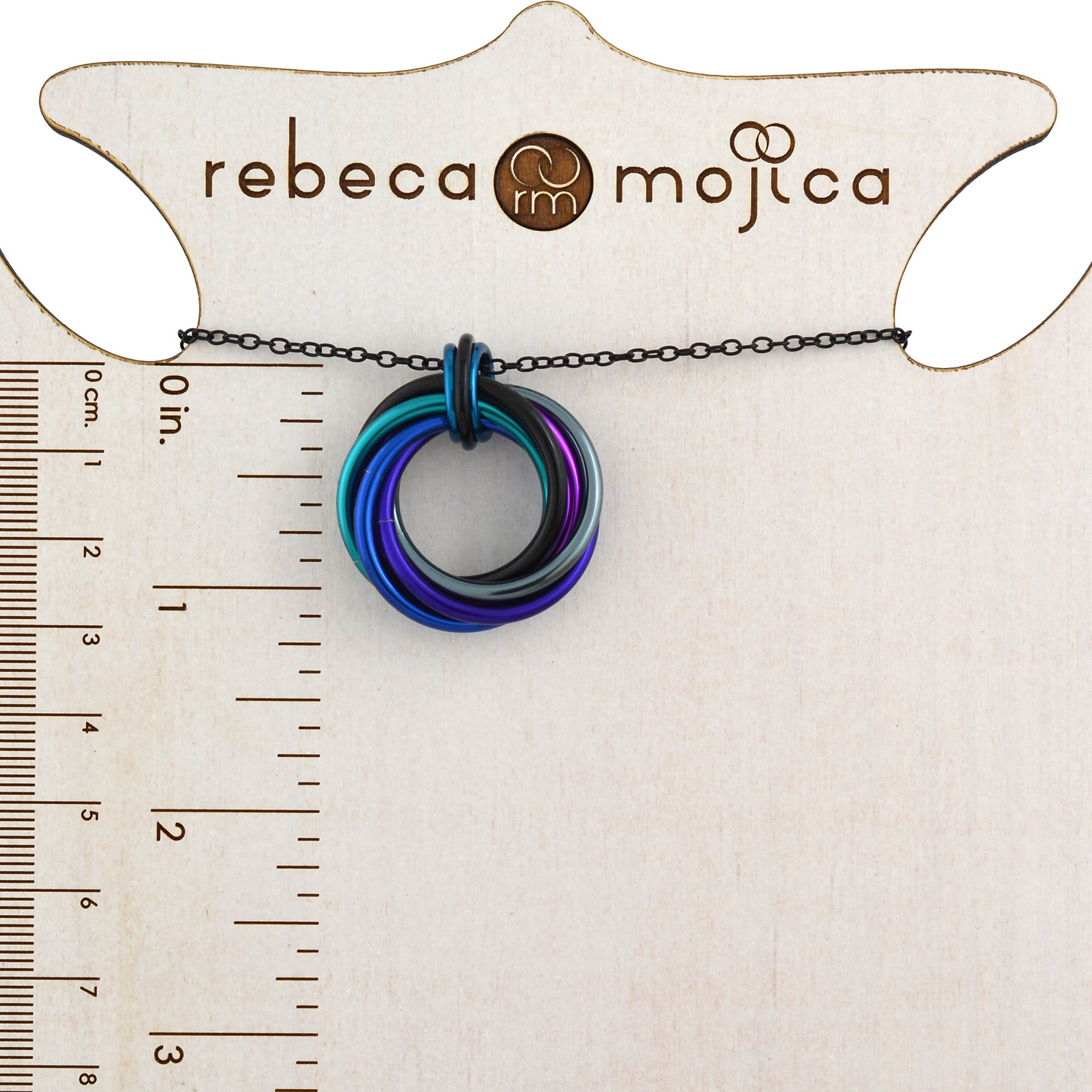 Size reference for the Swirl Pendant chainmaile necklace in Dark Mermaid colors on a branded wooden ruler display.
