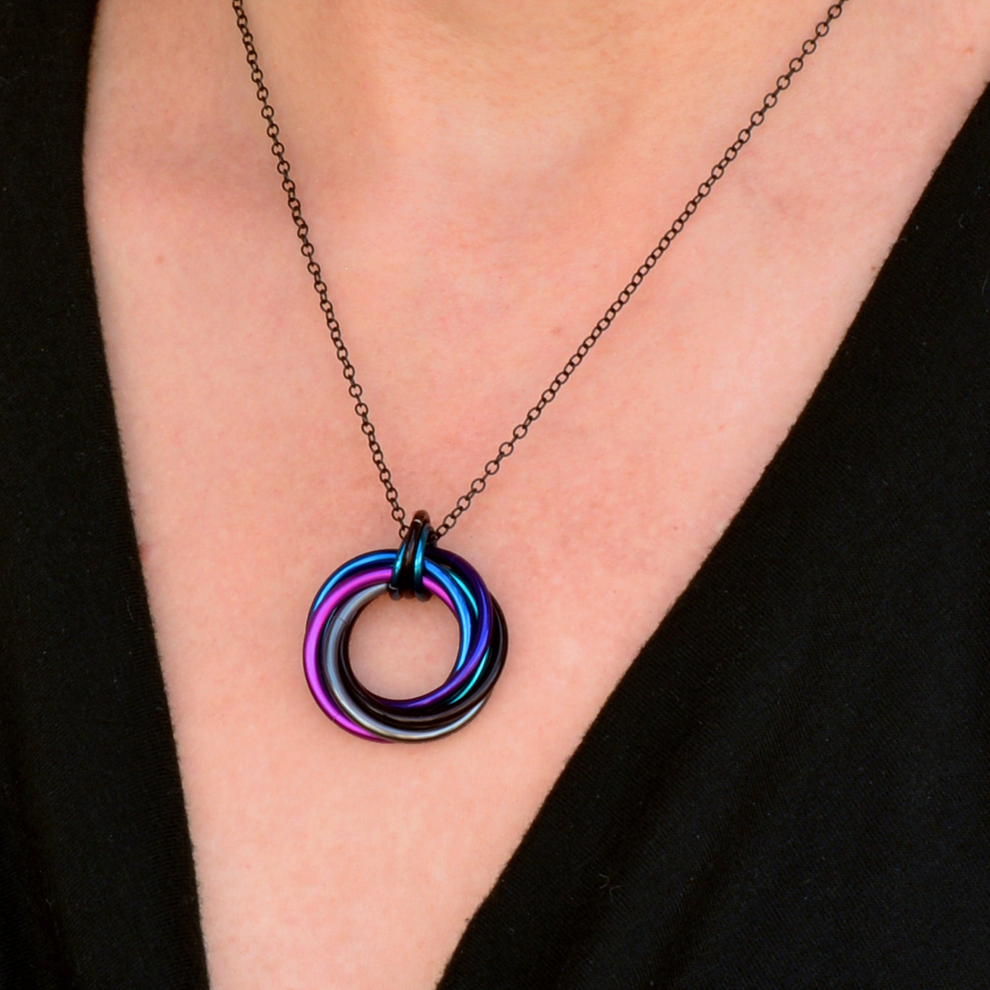 Close-up on the chest area showing the Swirl Pendant on a black chain, highlighting the intertwined rings and Dark Mermaid colors.