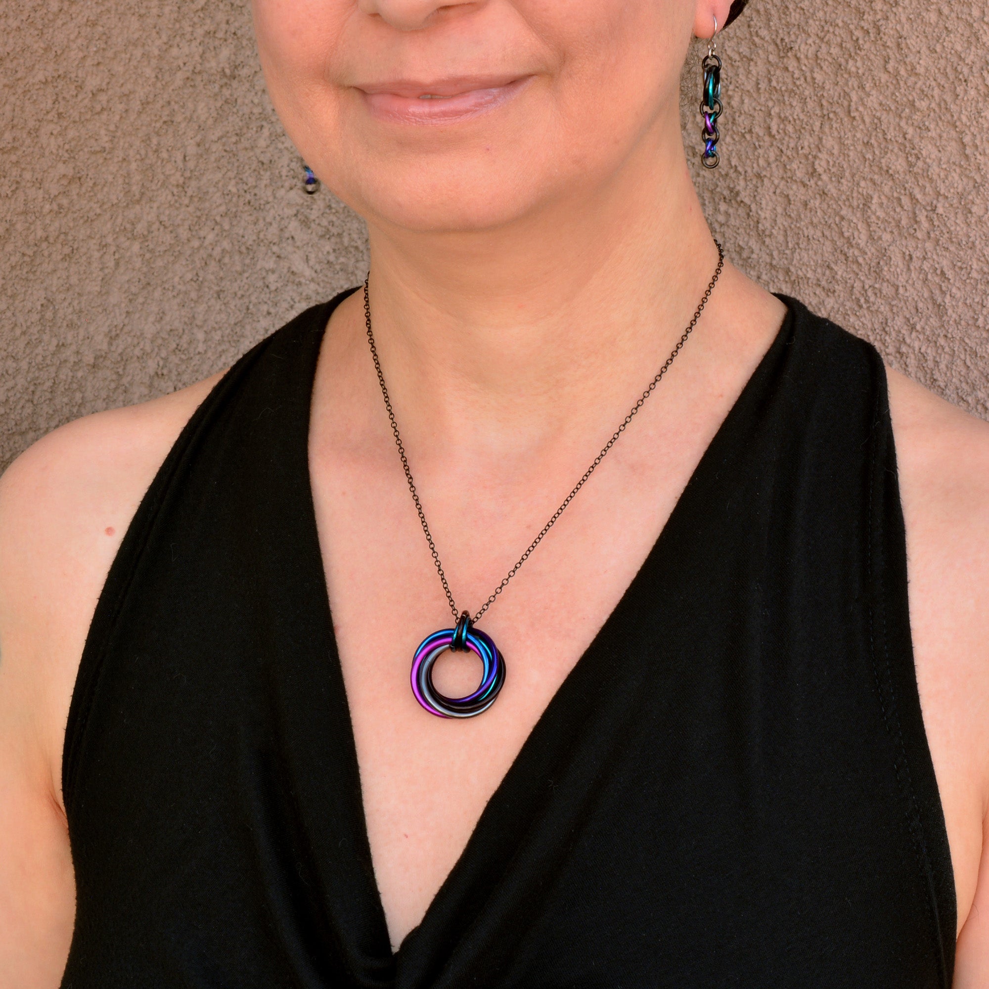 Close-up of Rebeca Mojica wearing the lightweight Swirl Pendant on a black chain, showing the vibrant, iridescent chainmaile pendant.