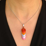 Closeup of chevron-style lesbian pride pendant on silver chain. Pendant is a series of stacked leaf-shaped metal components in anodized aluminum, each in a color of the lesbian flag. Pendant shown worn on a light-skinned person wearing a black top.