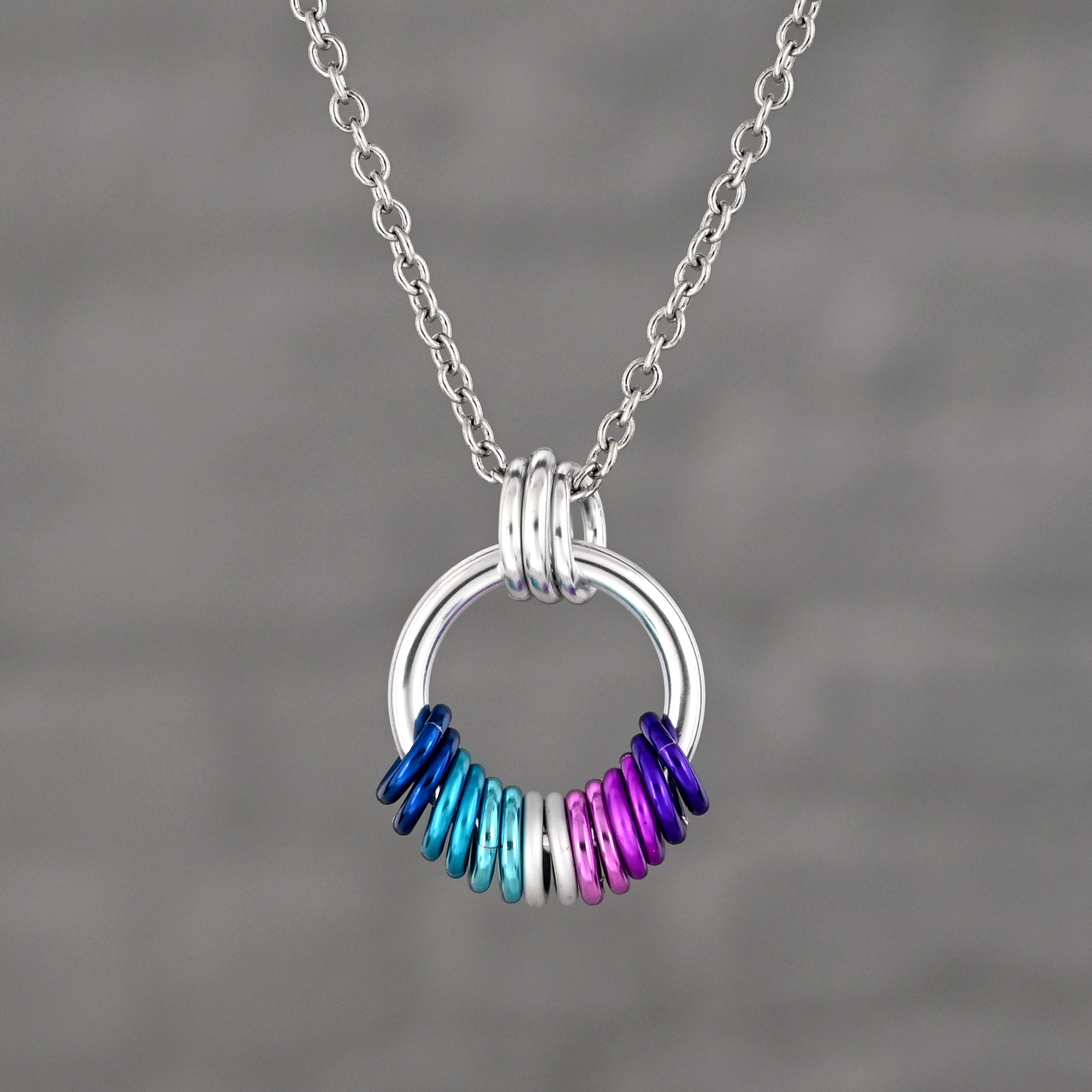  A silver-tone chainamille pendant with a coil of free-spinning rings in Berrisexual flag colors: a vibrant gradient of deep blue, cyan, white, violet and purple.
