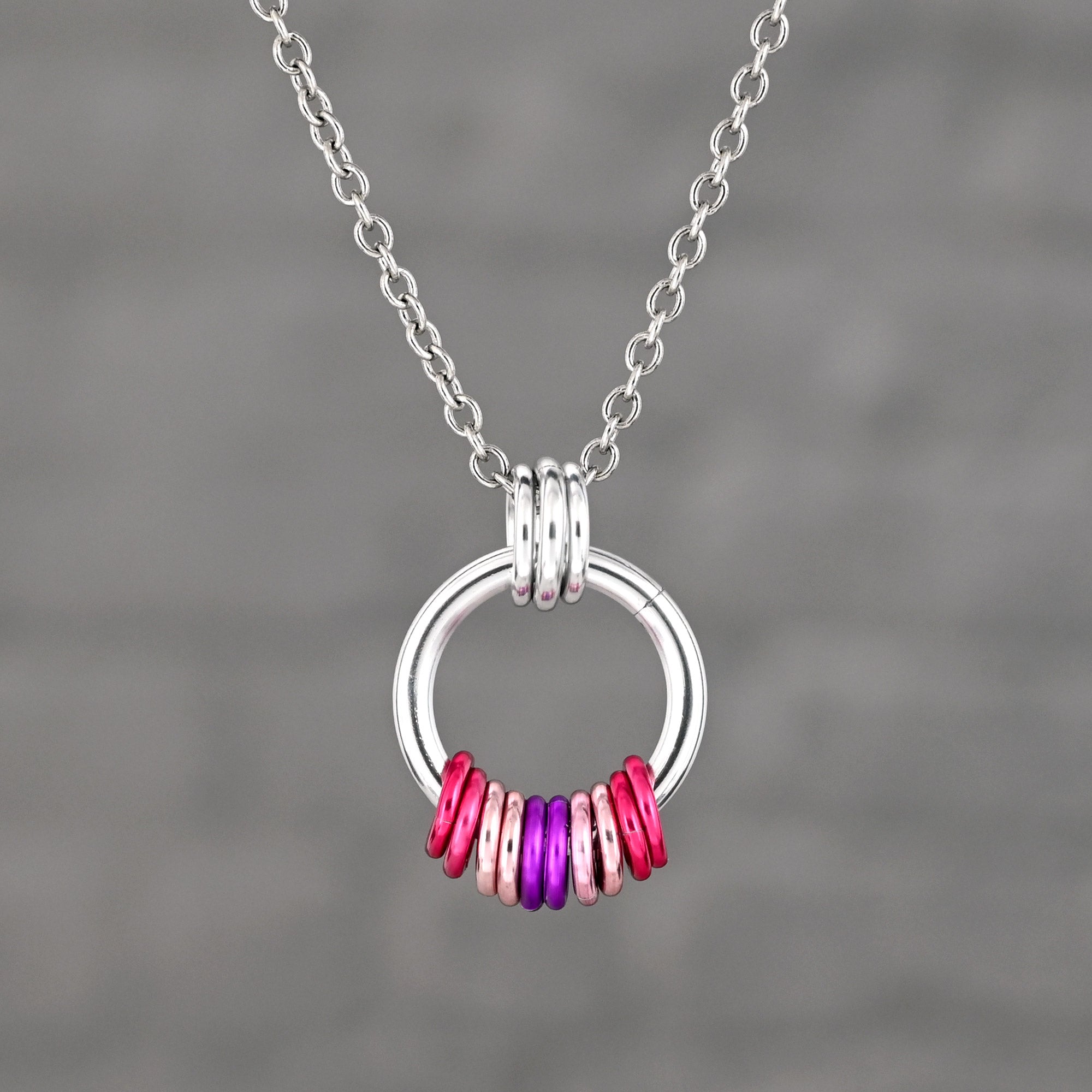A minimalist silver ring pendant with free-spinning aluminum rings in the Sapphic pride colors: shades of pink, white, and a purple-pink center.