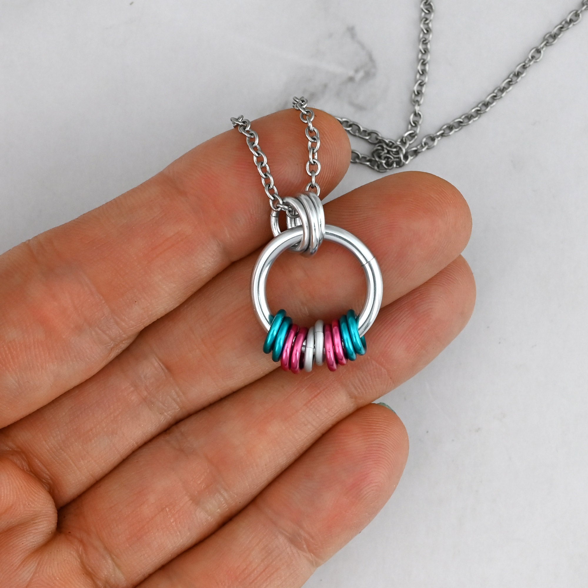 A close-up view of the Trans Pride pendant held in a hand for scale, showing the delicate silver chain and the smooth, vibrant finish of the blue, pink and white links of the transgender pride flag.