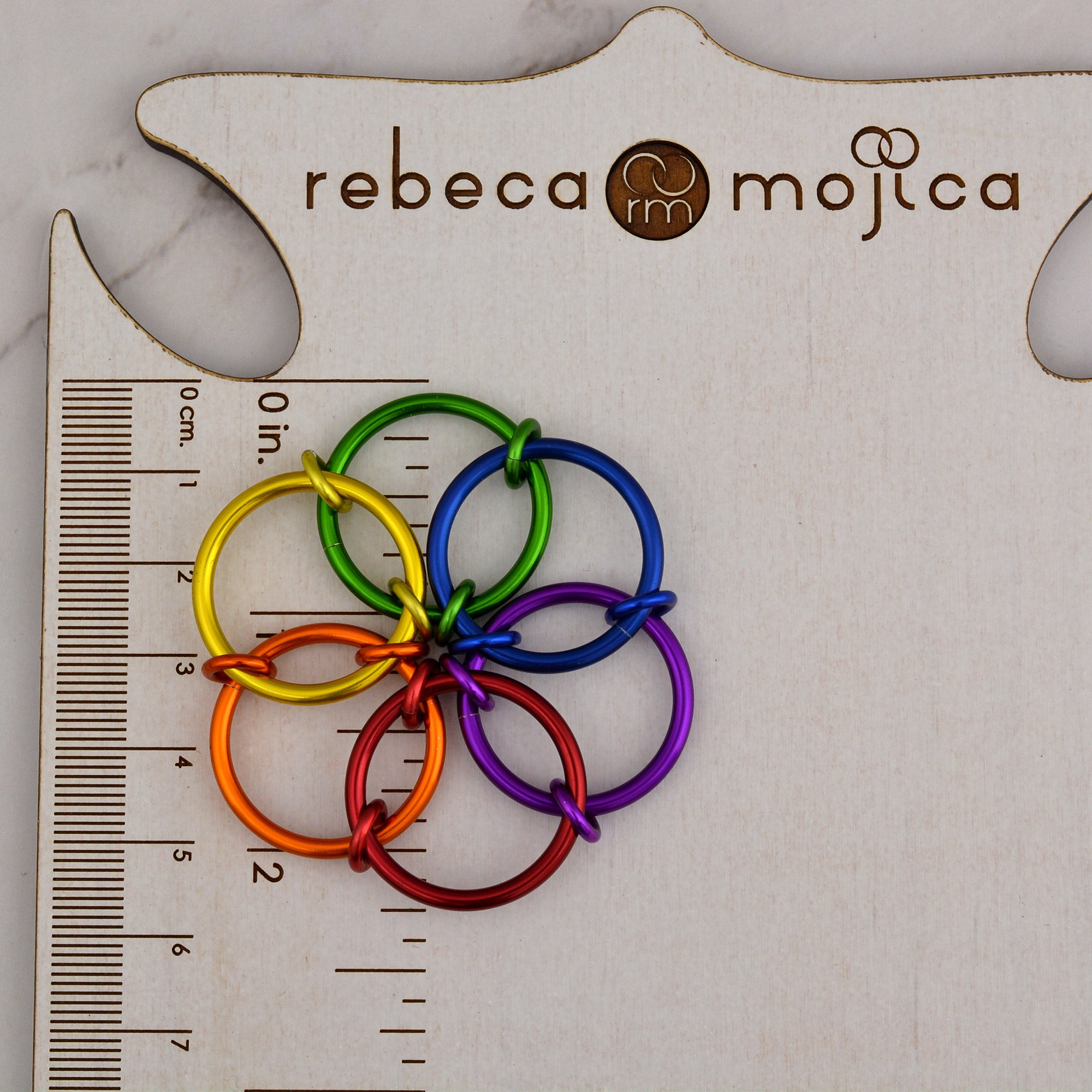A close-up view of the Rainbow Fidget Flower accessory on a branded jewelry card with a ruler, showing the flower's diameter is approximately 2.25 inches.