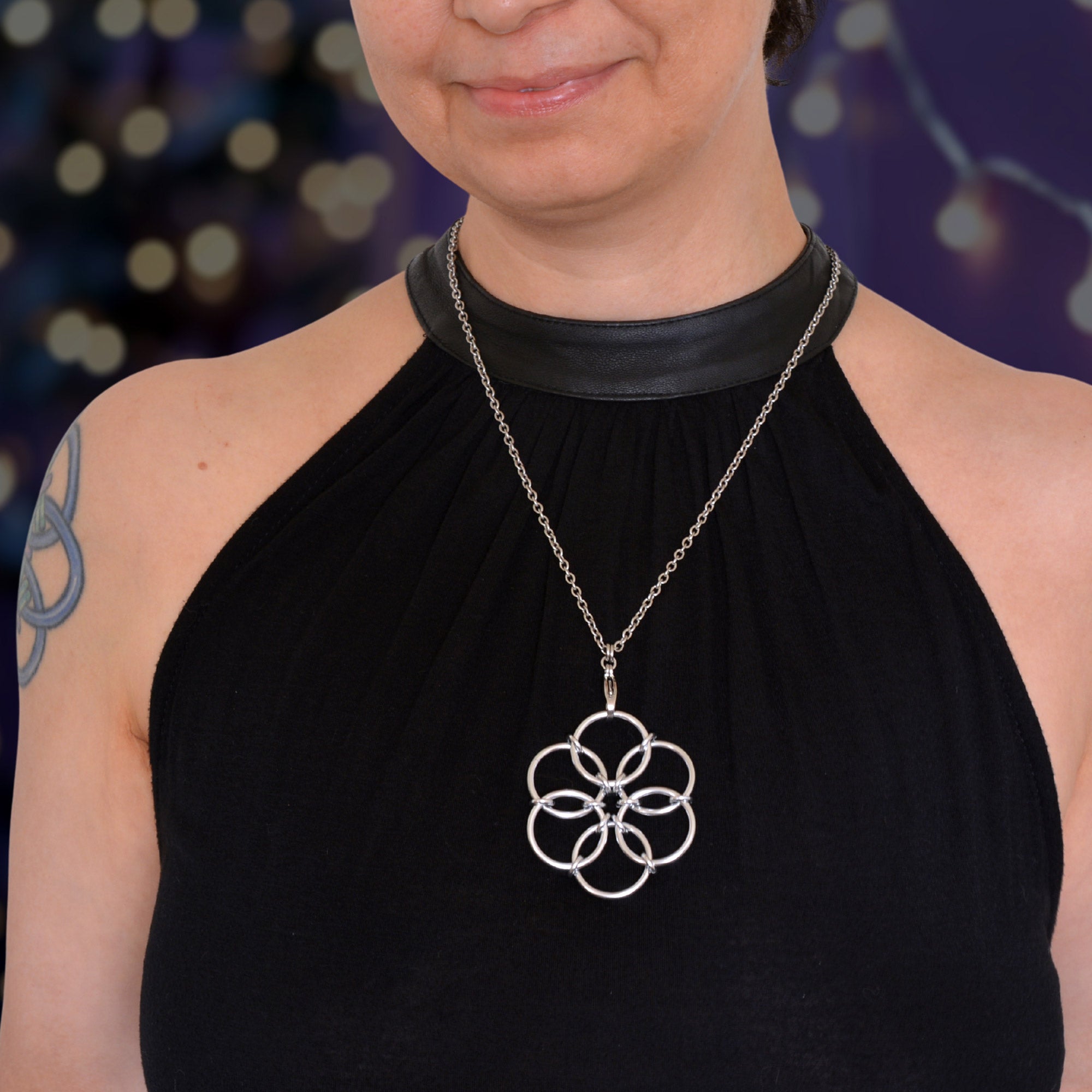 Lifestyle photo showing the artisan wearing the silver Fidget Flower necklace. The pendant hangs against a black halter top with a leather accent, illustrating the size and how the necklace is worn.