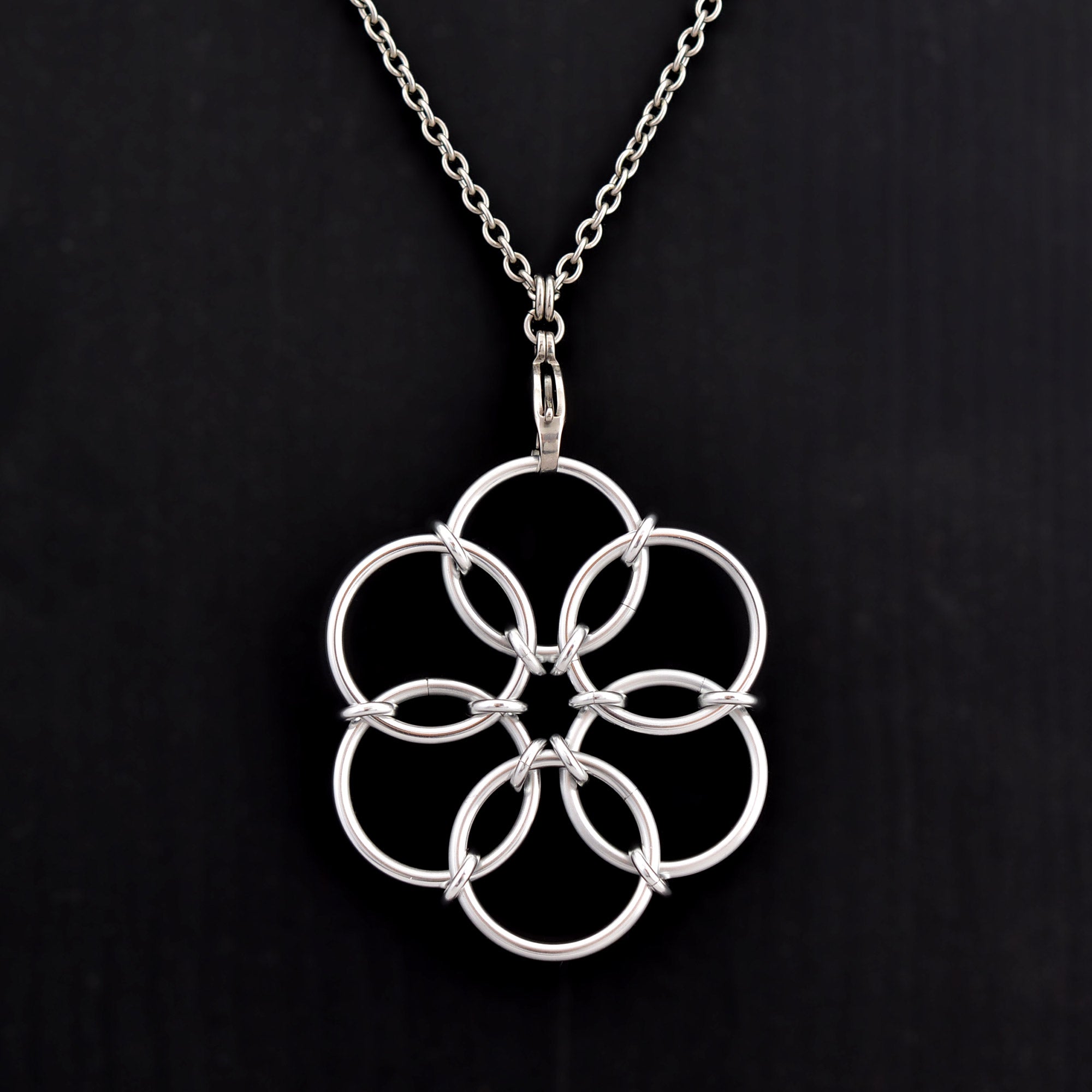 A close-up view of the silver color Fidget Flower necklace pendant resting against a solid black background.