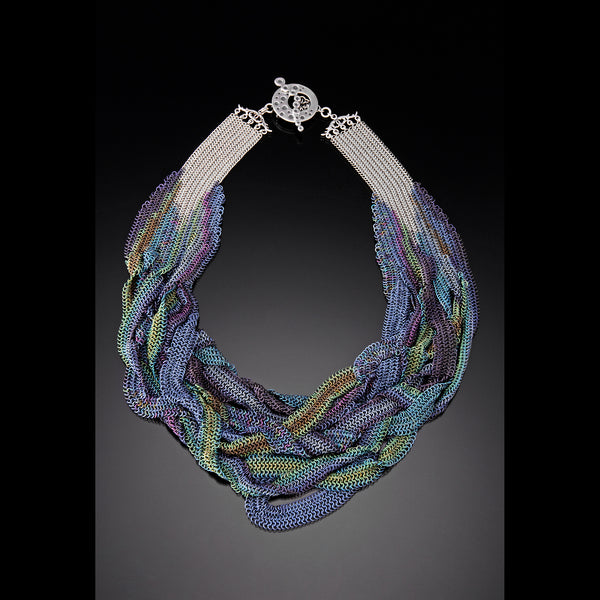 A high-fashion chainmaille necklace titled "Poseidon’s Embrace," featuring multiple draped strands of iridescent blue, green, and purple micromaille mesh with a silver toggle clasp, photographed on a reflective black surface
