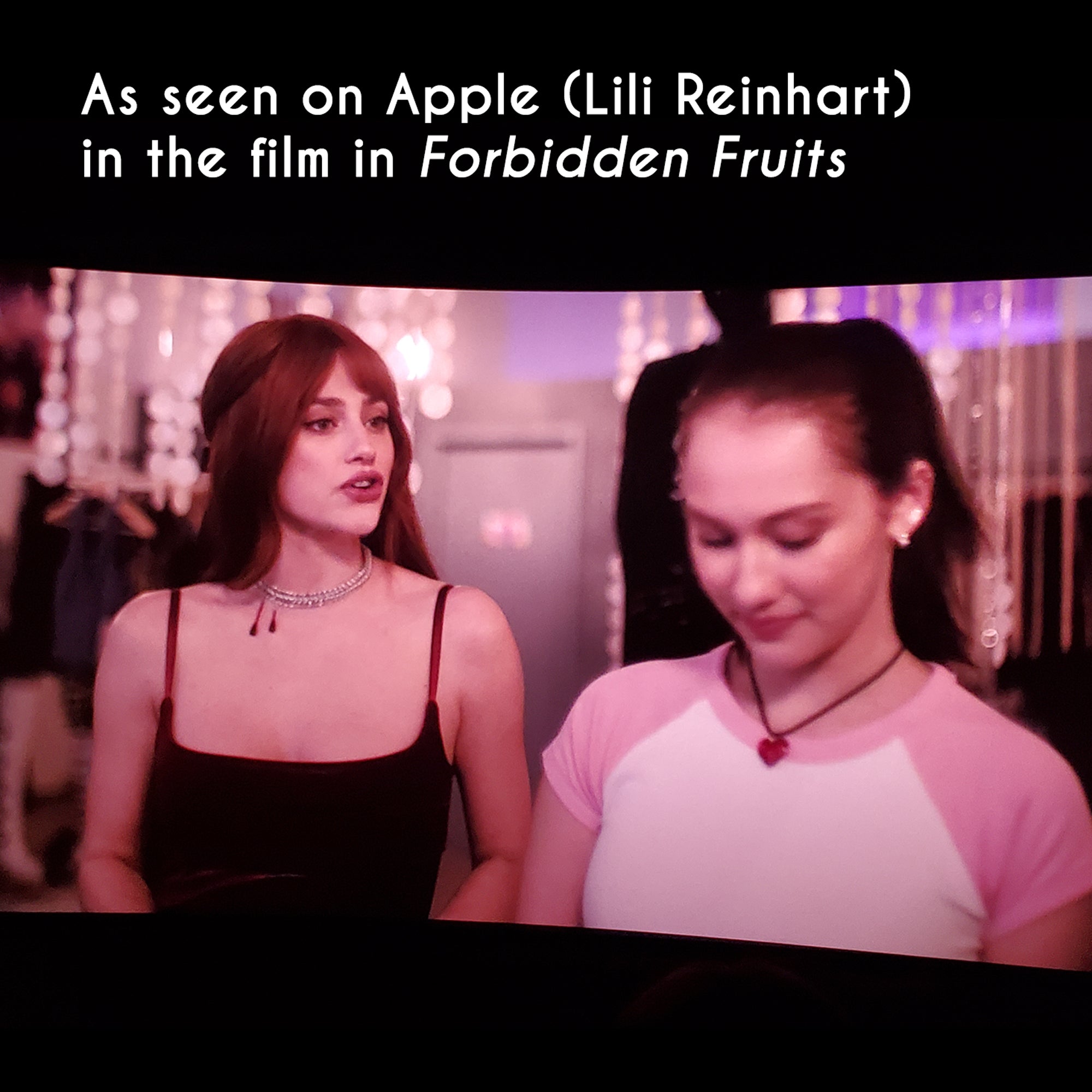 A square image featuring a wide-screen movie still from Forbidden Fruits. Actress Lili Reinhart (Apple) wears a Rebeca Mojica Vampire Bite chainmaille choker with red "blood" droplets. Beside her is actress Lola Tung (Pumpkin). Text at the top reads: "As seen on Apple (Lili Reinhart) in Forbidden Fruits."