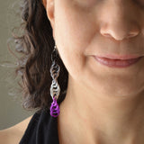 Closeup of the bottom right quadrant of a woman’s face wearing a long chainmaille spiral earring in the ace pride colors - black, grey, white and violet