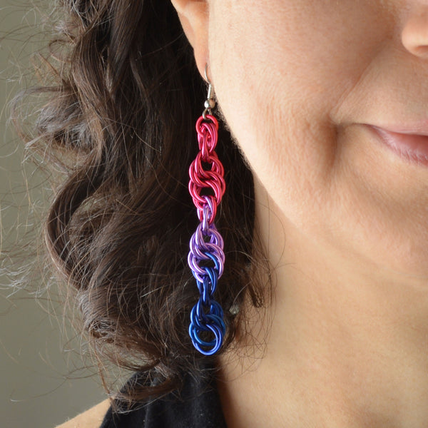 Closeup of the bottom right quadrant of a woman’s face wearing a long chainmaille spiral earring in the bi pride colors - pink, lilac, blue