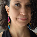 Artisan Rebeca Mojica wearing long chainmaille spiral earring in the pan pride colors - pink, gold and blue