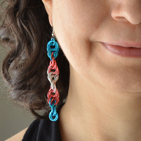 Closeup of the bottom right quadrant of a woman’s face wearing a long chainmaille spiral earring in the ace pride colors - blue, pink and white
