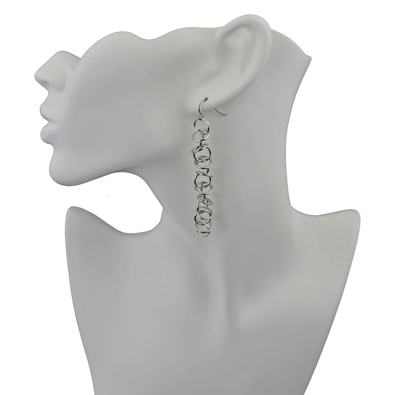 Long silver orbital earrings on white display form. 