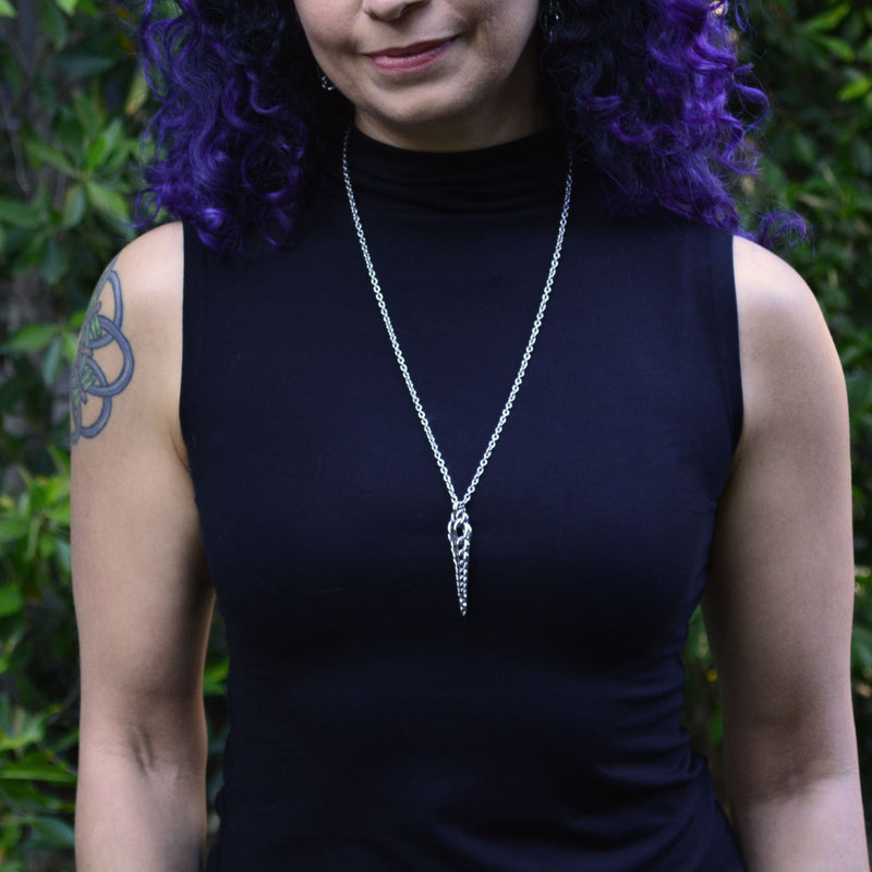 Auger Pendant by Rebeca Mojica worn long over a black top. Thin, stainless steel chainmaille pendant that has a slightly bulbous top and tapers to super teeny rings at the bottom tip.