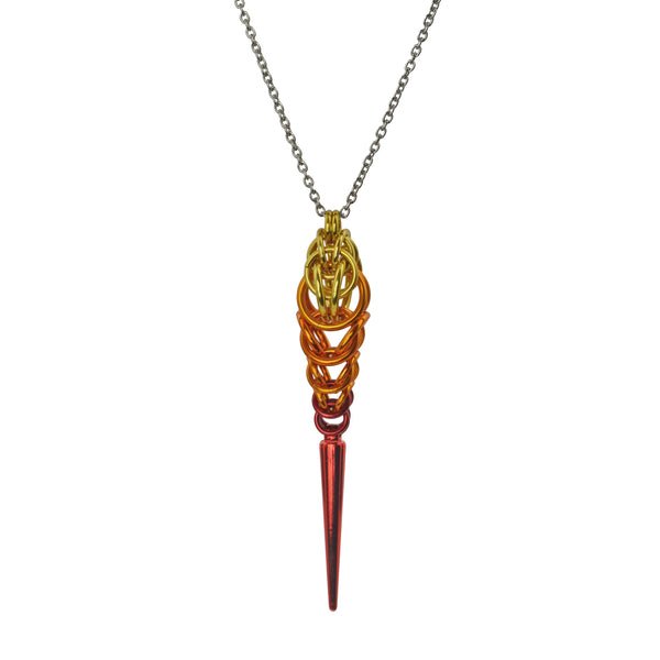 Chainmaille pendant resembling a flame with a spike at the bottom on a white background. Pendant is gold color at top, transitioning to orange and finally red, with a long red spike at the base.