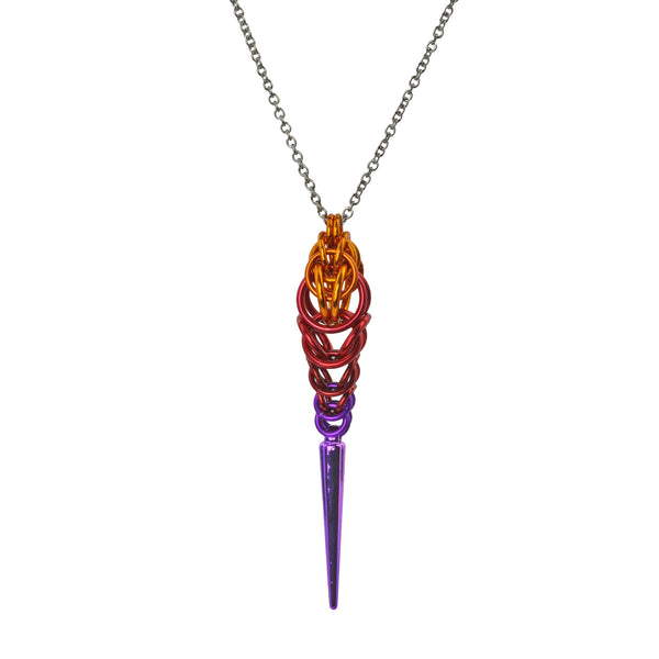 Chainmaille pendant in an ombre with a spike at the bottom on a white background. Pendant is orange color at top, transitioning to red and finally violet, with a long violet spike at the base.
