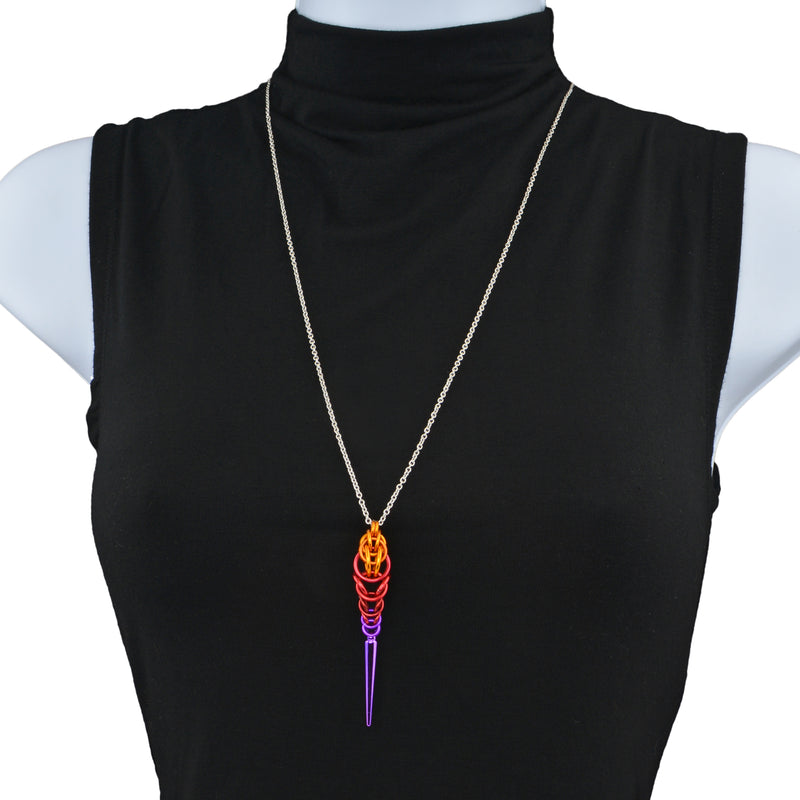 Chainmaille pendant on a stainless steel chain displayed on a torso form with a black turtleneck shirt. The pendant is made of chainmaille and is orange at the top, red in the middle and violet at the bottom, with a long violet spike at the base.
