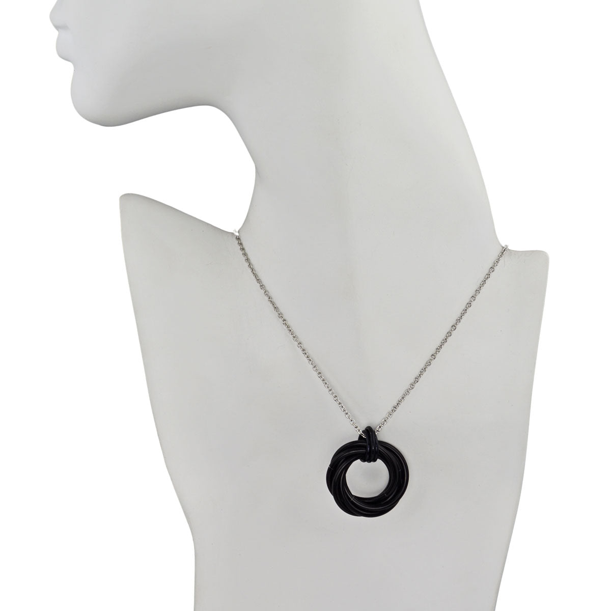 A black chainmaille swirl pendant hangs from a silver-colored chain on a white mannequin's neck and upper torso, showcasing how the necklace lays when worn.