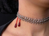 Closeup of neck with silver color chainmaille mesh band and two deep red drops meant to look like blood trickles. The red drops are positioned on the side of the neck, to allude to a vampire bite. 